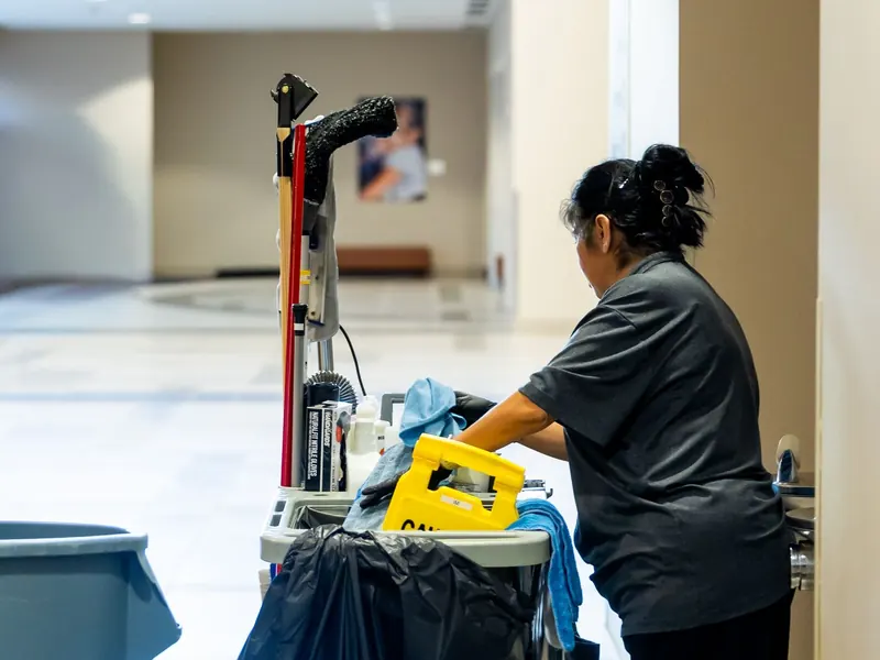 Janitorial worker with a cleaning cart in a building hallway