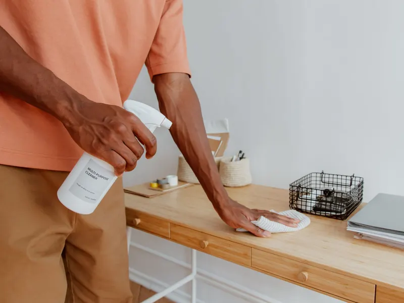 Person wiping down a desk with a cloth and spray bottle